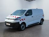 La camionnette blanche est garée dans une pièce blanche, avec un autocollant à carreaux rouges et blancs sur le côté.