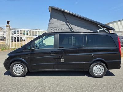 une camionnette noire garée sur un parking, avec une tente posée sur le toit