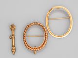 deux broches en or et une épingle posées sur un fond gris