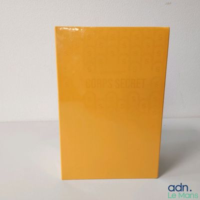 un livre orange posé sur une table blanche, près d'un mur blanc