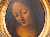 painting of a woman ' s face in a gold frame on a wall