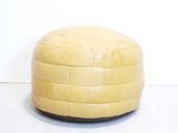 yellow leather pouffe sitting on a white floor in front of a white wall