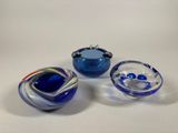 three blue glass bowls with swirl designs on them sitting on a white surface