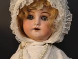 a close up of a doll wearing a white dress and a bonnet