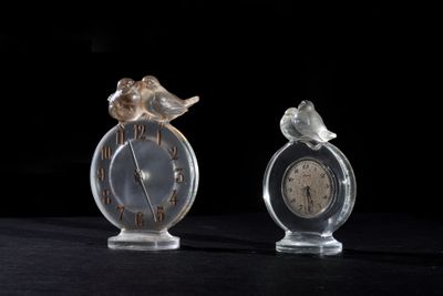 two small glass clocks with birds on them on a table