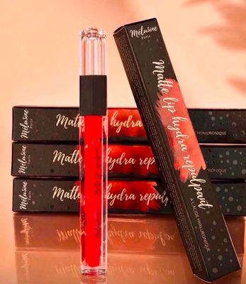 Trois gloss sont posés sur une table, à côté d'une boîte de rouges à lèvres