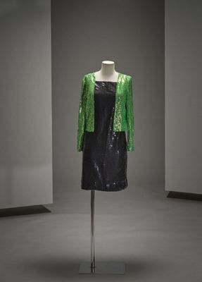 une robe noire ornée de paillettes vertes, posée sur un présentoir pour mannequin