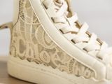 beige lace high top sneakers on a wooden surface with a white background