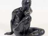 une sculpture noire représentant un homme assis par terre, les mains posées sur les genoux