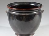 a black vase with a brown rim sitting on a white surface