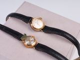 une paire de montres à bracelet en cuir noir et boîtier doré sur fond blanc