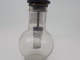 un bocal en verre muni d'une poignée en métal posé sur une surface blanche