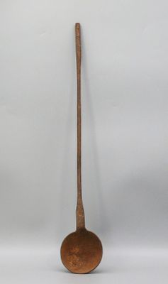 une vieille cuillère en bois à long manche posée sur une surface blanche
