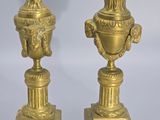 pair of antique brass vases on pedestals against a gray background