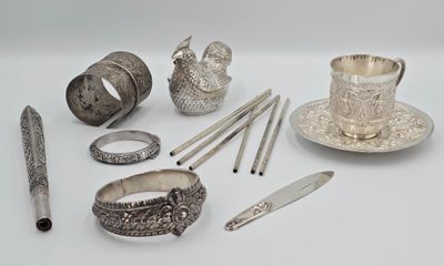 de nombreux objets en argent posés sur une surface blanche, notamment une tasse à thé, une cuillère et d'autres objets