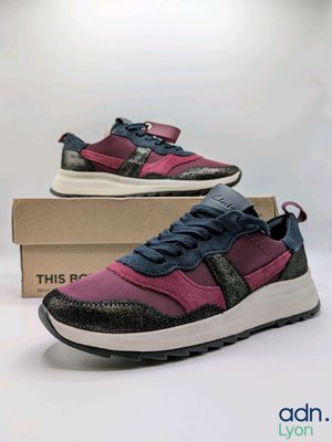 Les baskets violettes et noires se trouvent dans une boîte posée sur une surface blanche.
