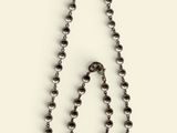 a close up of a metal beaded necklace on a white surface