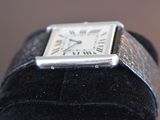a small silver square watch on a black velvet case