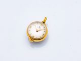 une petite montre de poche en or posée sur une surface blanche