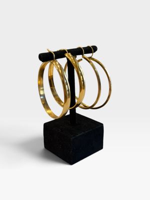 trois boucles d'oreilles en anneau dorées posées sur un support noir, sur fond blanc