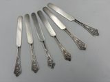 six silverplated knives and a knife on a white surface