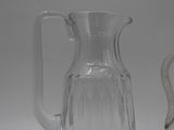 a clear glass pitcher and a silver pitcher on a table