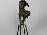 une statue en bronze représentant une femme assise sur un tabouret, la main posée sur le menton
