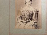 an old photo of a woman in a dress sitting on a chair