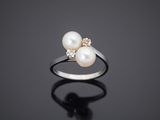 a white pearl and diamond ring on a black surface