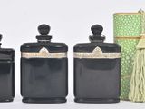 three black jars with tassels and a green box on a white surface
