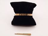 une photo représentant un bracelet en or et un stylo posés sur un sac en velours noir