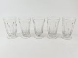 six clear shot glasses lined up in a row on a white surface