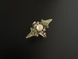 un gros plan d'une bague en or ornée d'une perle et de feuilles vertes