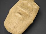 un petit objet en pierre sur lequel est représenté un visage, sur un fond noir