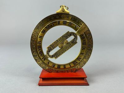 une vieille horloge en laiton posée sur un socle rouge, avec des chiffres romains