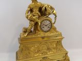 a gold clock with a man sitting on top of it