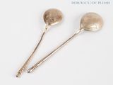two silver spoons sitting next to each other on a white surface