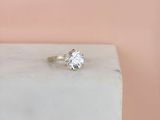 une image représentant une bague en diamant posée sur un bloc de marbre blanc