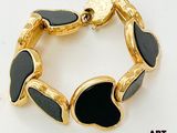 une image représentant un bracelet noir et doré posé sur une surface blanche