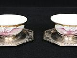 une paire de tasses et soucoupes plaquées argent, ornées de fleurs roses
