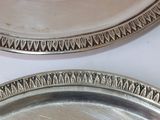 two silver plates on a white table with silver trimming