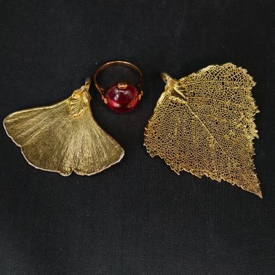 un gros plan sur une paire de boucles d'oreilles en feuille d'or ornées d'une perle rouge