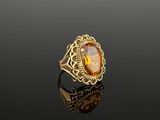 a gold ring with an oval citrine stone surrounded by a filigree band