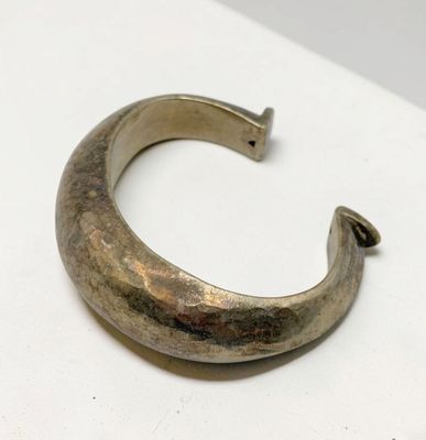 un vieux bracelet en argent présentant un motif incurvé sur une surface blanche