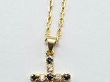 un pendentif en forme de croix en or, orné de pierres noires et blanches, monté sur une chaîne