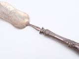silver plated serving spoon with ornate handle on a white surface