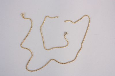 un collier en or dont la chaîne a été coupée en deux et qui repose sur une surface blanche
