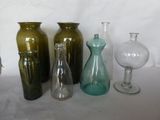 Plusieurs vases en verre sont alignés sur une table devant un fond blanc.
