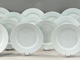 twelve white dinner plates are lined up in a row on a table