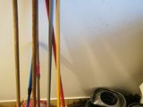 several brooms and mops are lined up on the floor next to a trash can